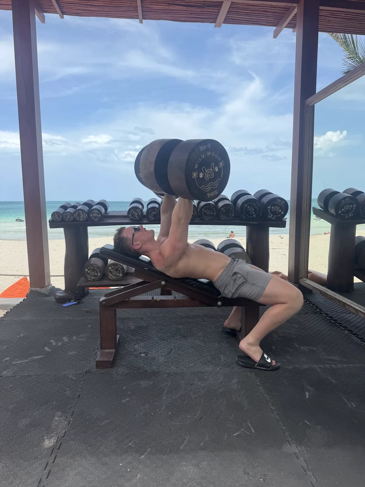 Bench pressing a wooden log dumbbell overlooking the ocean at Wild Wood Beach Fitness, Ko Samui